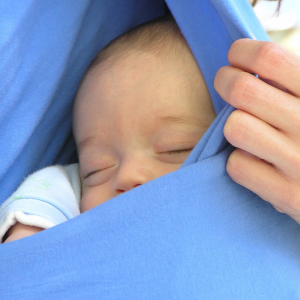 תינוק קטן ישן בתוך מנשא כחול צמוד לאמא שלו